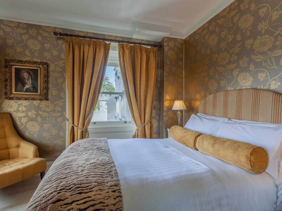 Ein Hotelzimmer mit Bett, Stuhl, Lampe und einem Fenster mit Vorhängen.