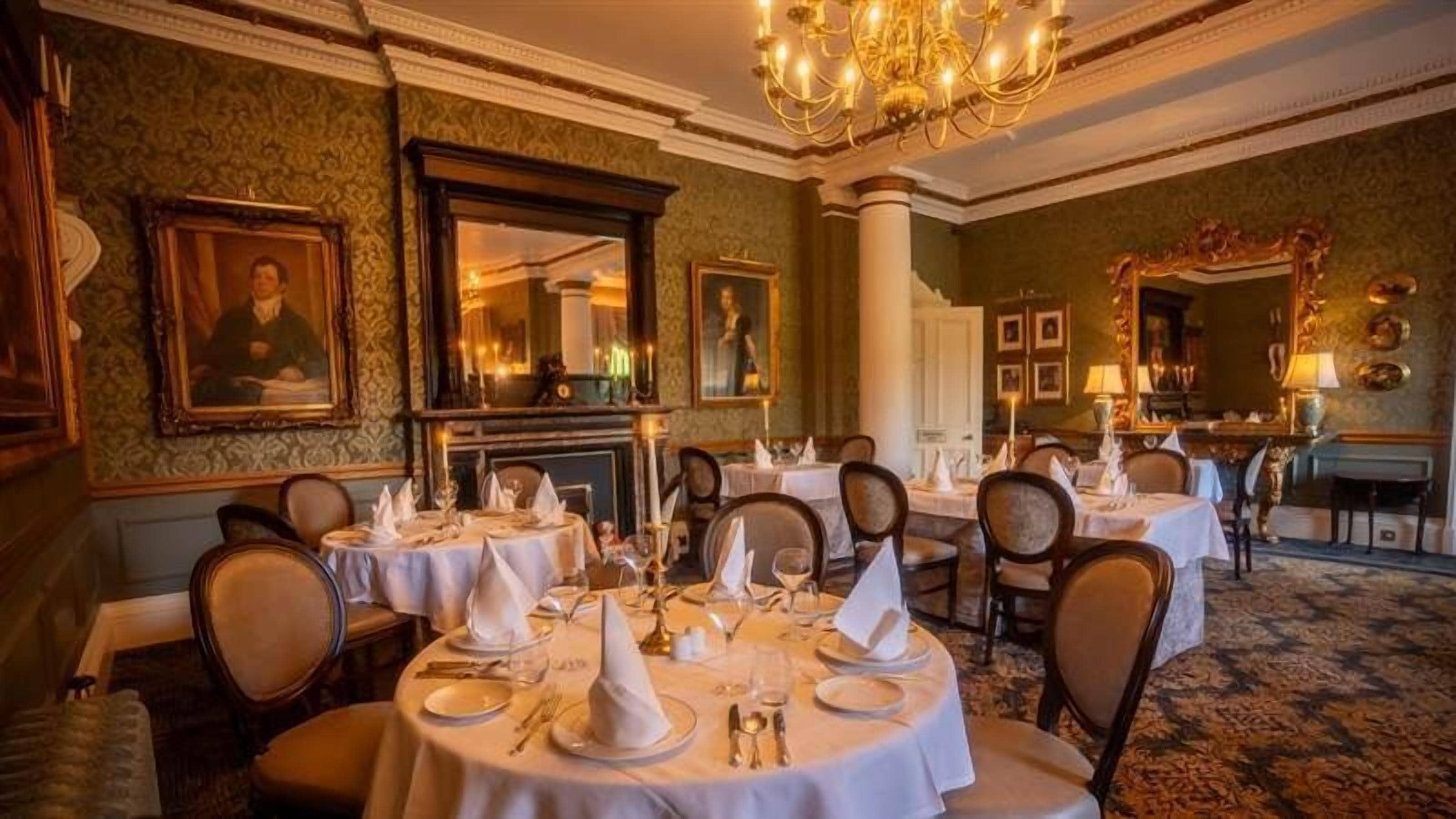 Une salle à manger formelle avec des tables rondes dressées pour le service, des chaises élégantes et un lustre.