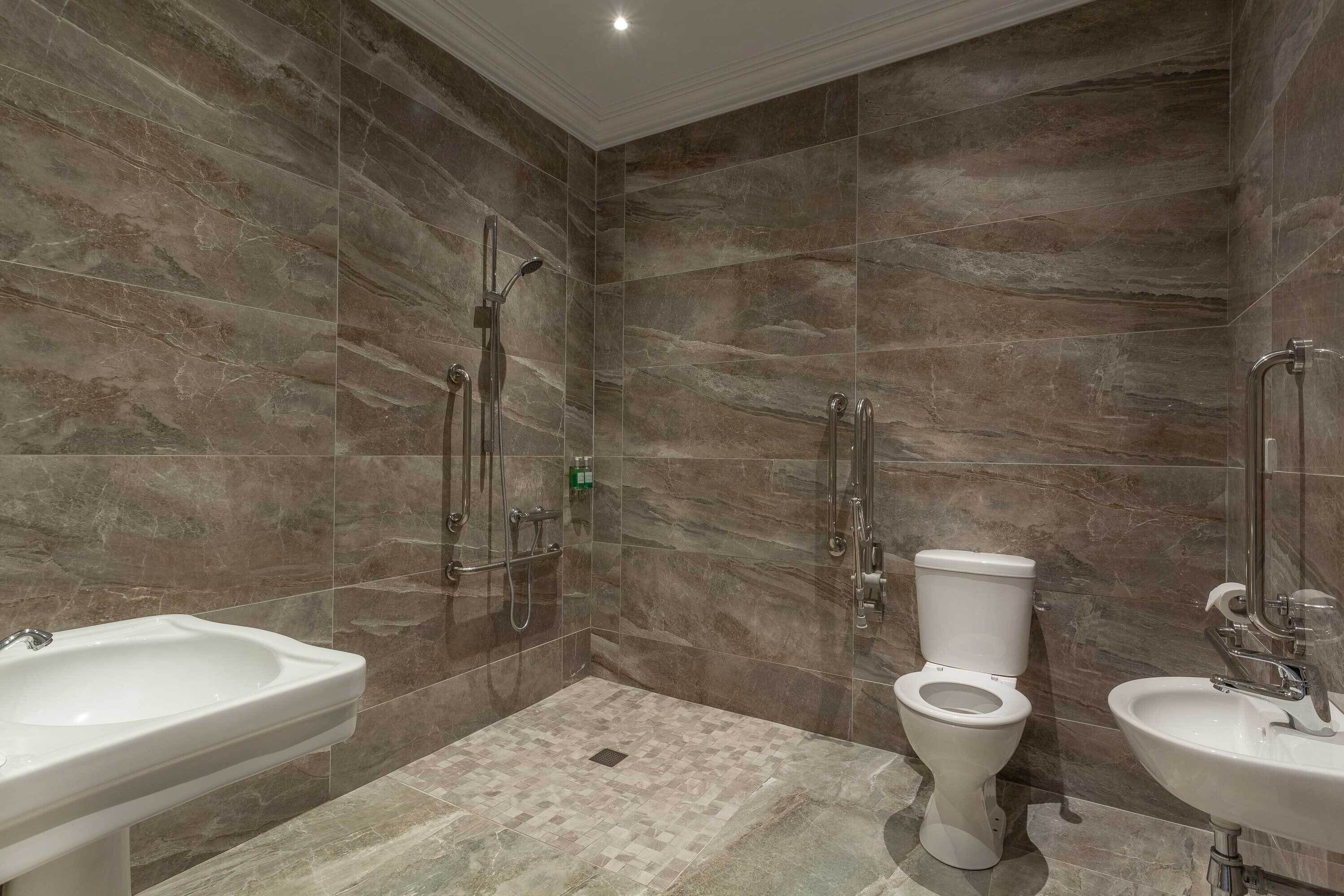 Een moderne badkamer met een douche, toilet en twee wasbakken.