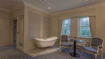 A room with a freestanding bathtub, patterned carpet, and two upholstered chairs.