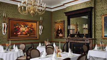 Een formele eetzaal met meerdere gedekte tafels, een groot bloemschilderij en een portret aan de muur.