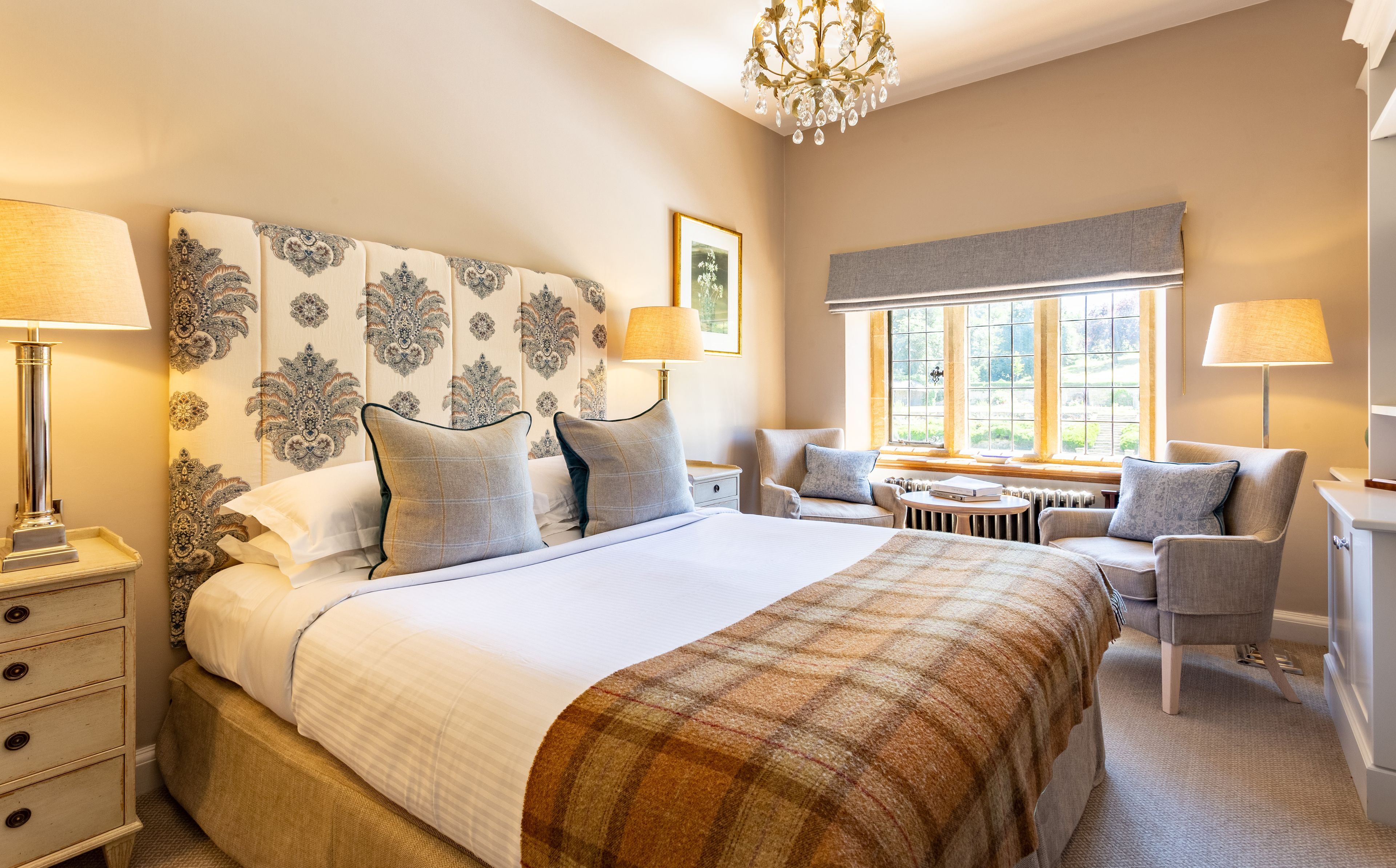 A well-lit bedroom with a large bed, two bedside tables, a chair, and a window with a view.