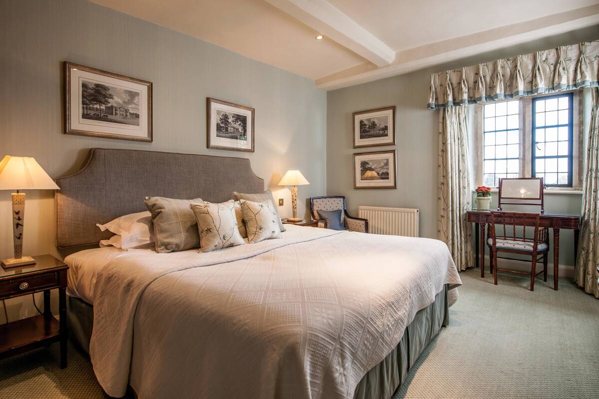 Une chambre à coucher bien rangée, avec un grand lit, deux tables de chevet avec des lampes, un bureau en bois et des tableaux encadrés accrochés aux murs.
