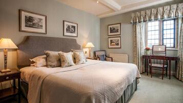 A neatly arranged bedroom with a large bed, two bedside tables with lamps, a wooden desk, and framed pictures on the walls.