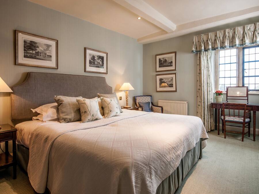 A neatly arranged bedroom with a large bed, two bedside tables with lamps, a wooden desk, and framed pictures on the walls.