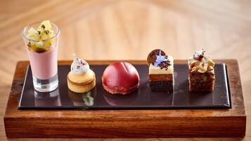 Una bandeja de postres con diversas golosinas, incluyendo una bebida rosa, un macaron rojo, un profiterole blanco, un postre de chocolate y un pastel en capas.