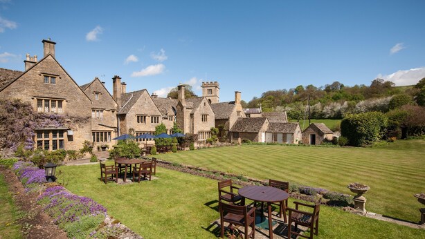 A traditional stone building with multiple chimneys, a well-maintained lawn, and outdoor seating areas. - Buckland Manor (Broadway)