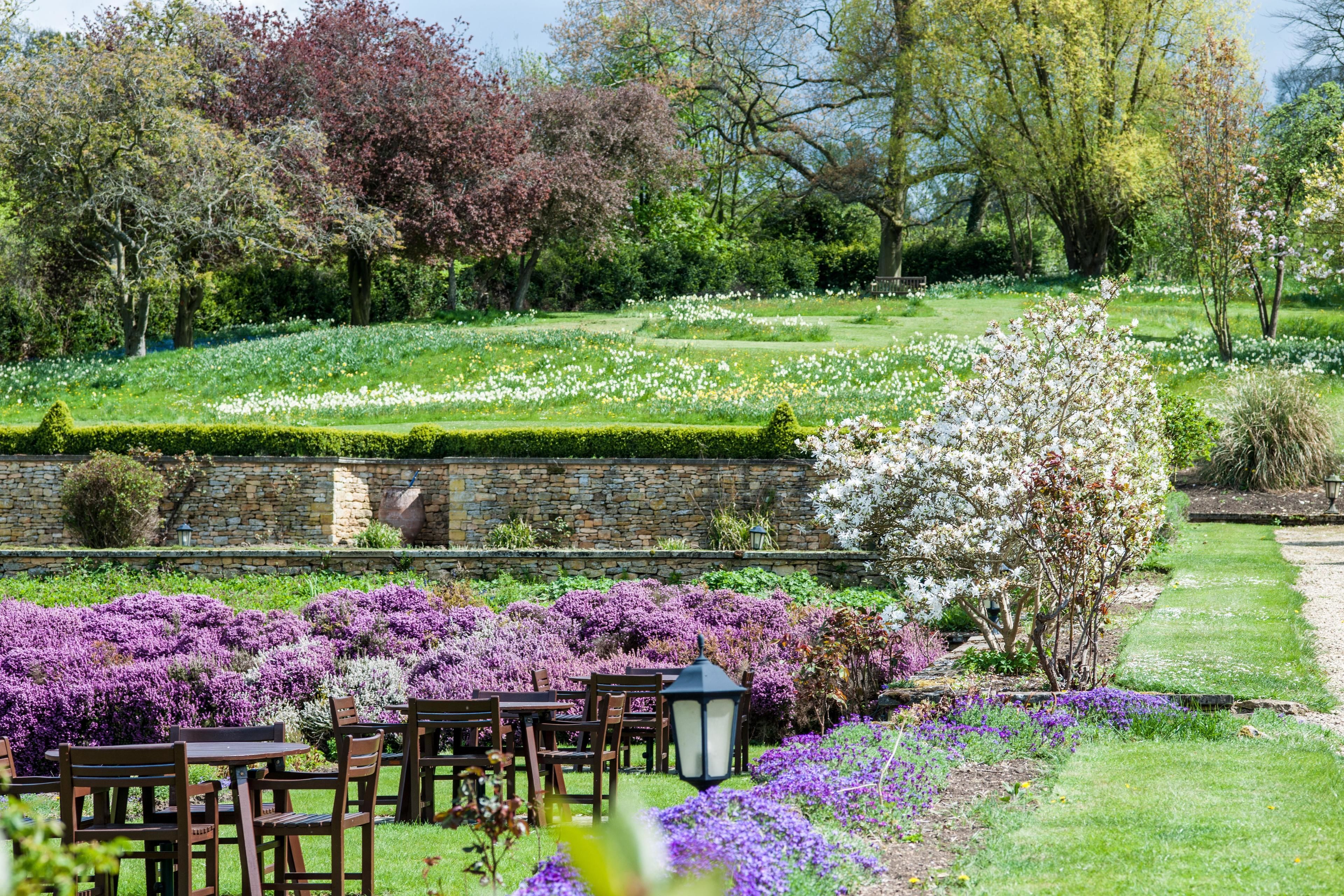A garden with a dining area, stone wall, and various flowering plants.