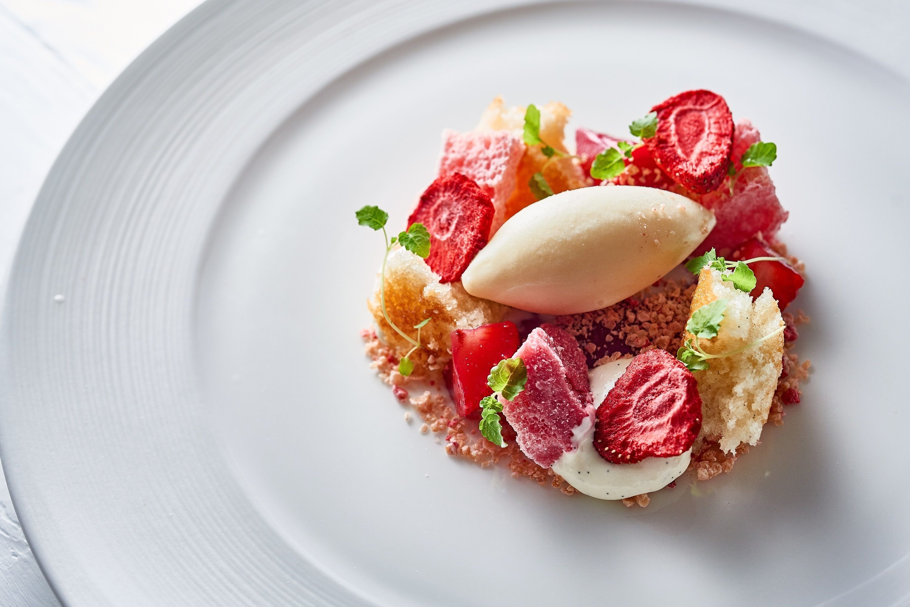 A dessert on a white plate with strawberries, mint, and a scoop of ice cream.