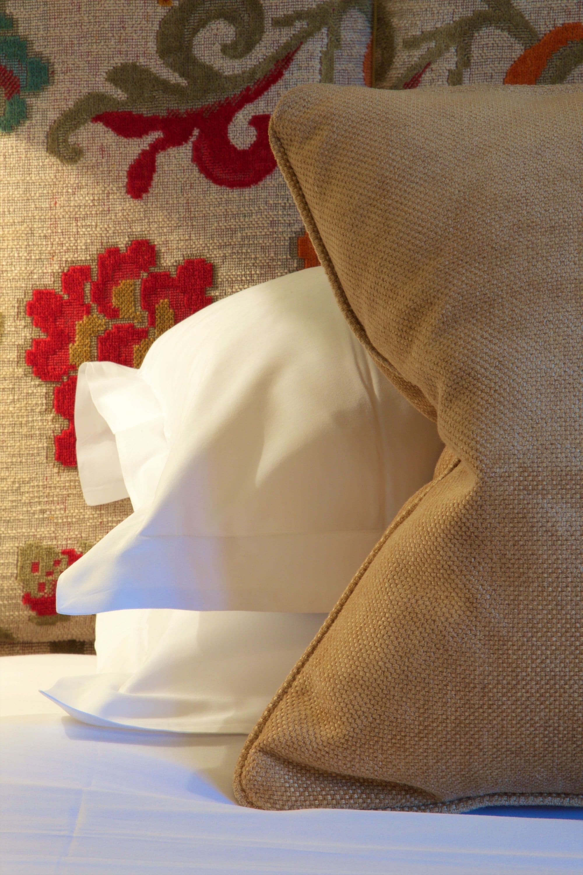 A bed with a white pillow and a beige pillow against a patterned wall.