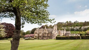 A large, historic building with a symmetrical facade, surrounded by well-manicured lawns and mature trees. - Buckland Manor (Broadway)