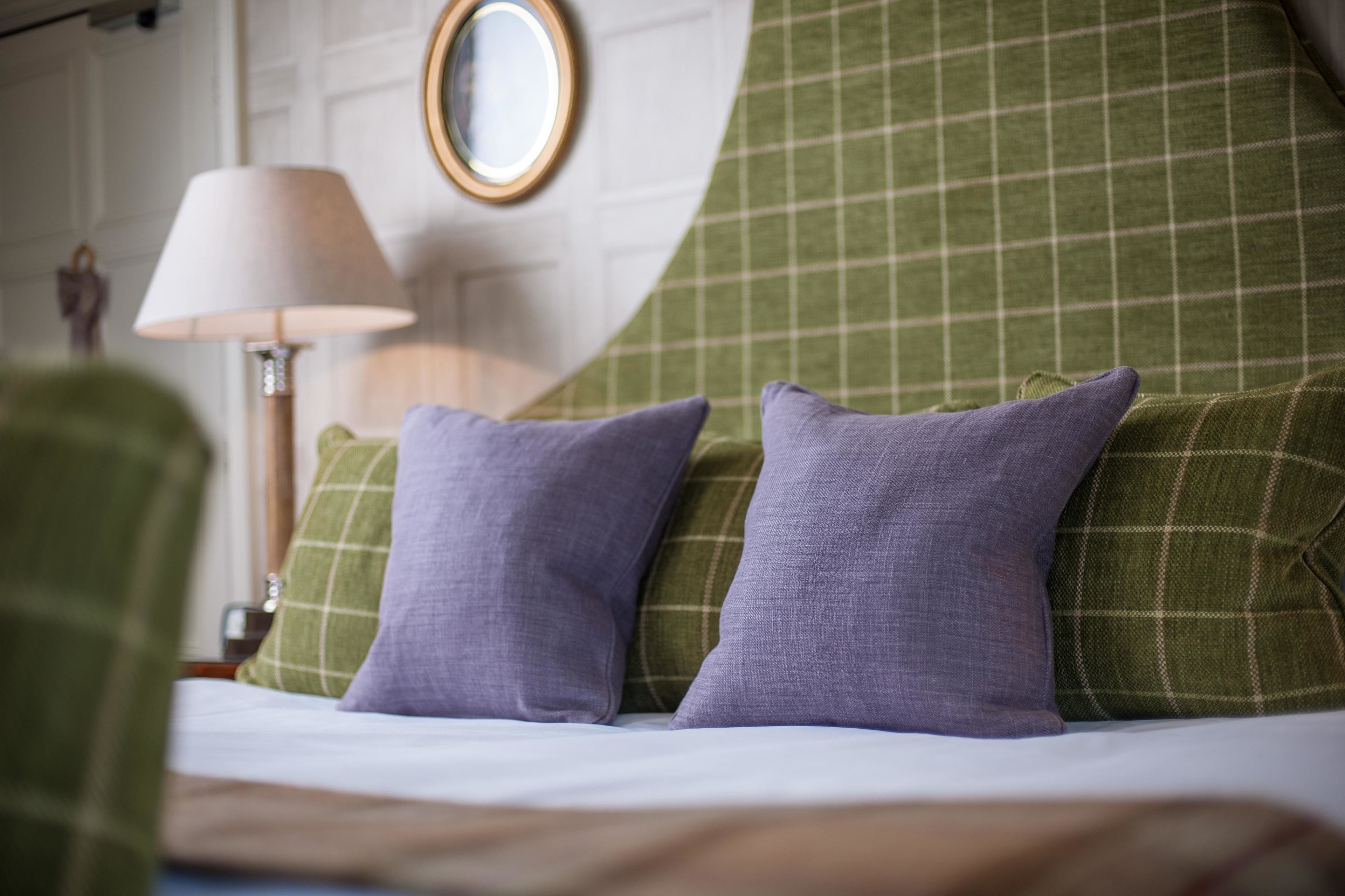 Una cama con almohadas verdes y moradas, una lámpara y un espejo en la pared.