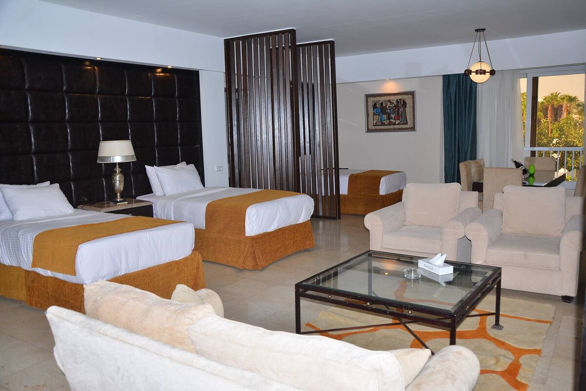 A hotel room with two beds, a sofa, a coffee table, and a view of the outdoors.