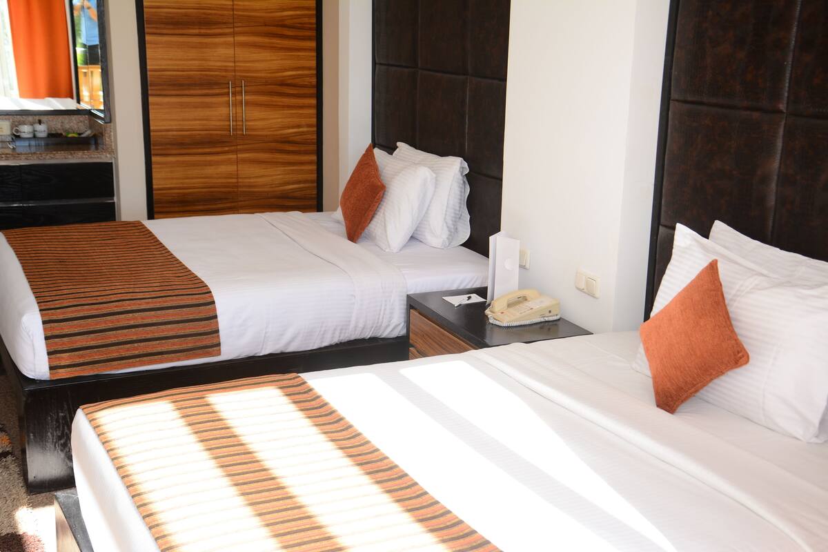 Two adjacent beds with striped bedspreads, a wooden wardrobe, and a nightstand with a telephone and a tissue box.