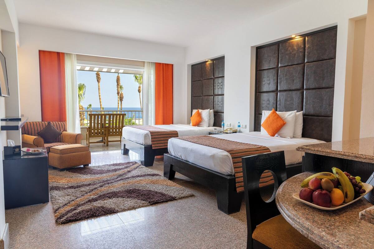 A hotel room with two beds, a sofa, a dining table, and a view of the ocean.