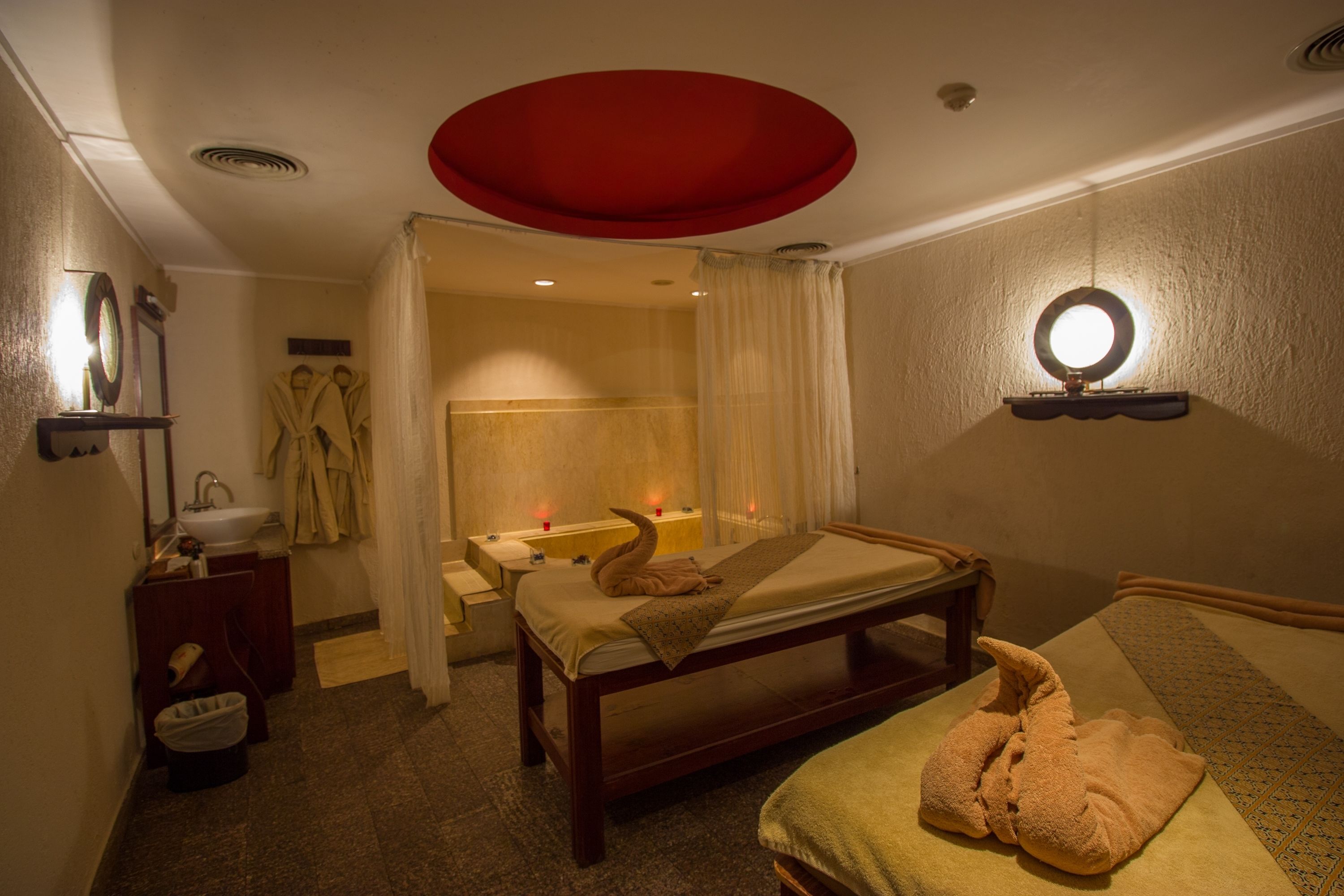 Ein Hotelzimmer mit Bett, Nachttisch, Spiegel, Badezimmer mit Dusche und einer roten Deckenleuchte.