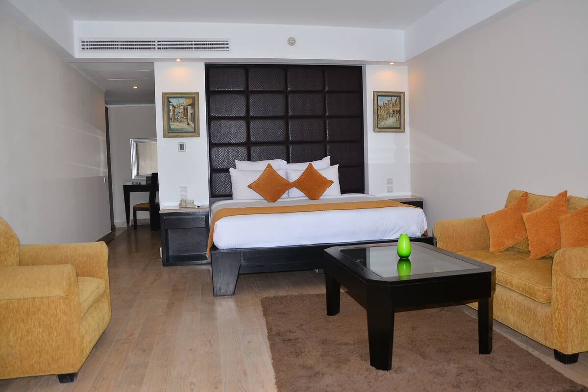 A hotel room with a large bed, two sofas, a coffee table, and artwork on the walls.