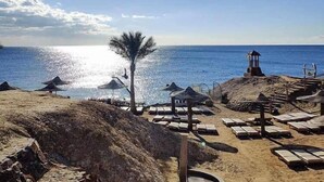 A beach with sun umbrellas, lounge chairs, and a lifeguard tower.