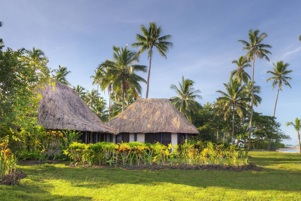 Ein tropisches Resort mit strohgedeckten Hütten, umgeben von üppiger Vegetation und Palmen.