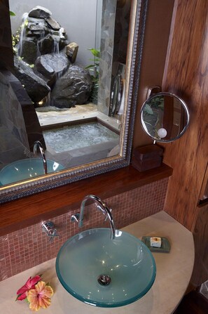 A bathroom with a glass sink, a mirror, and a small waterfall feature.