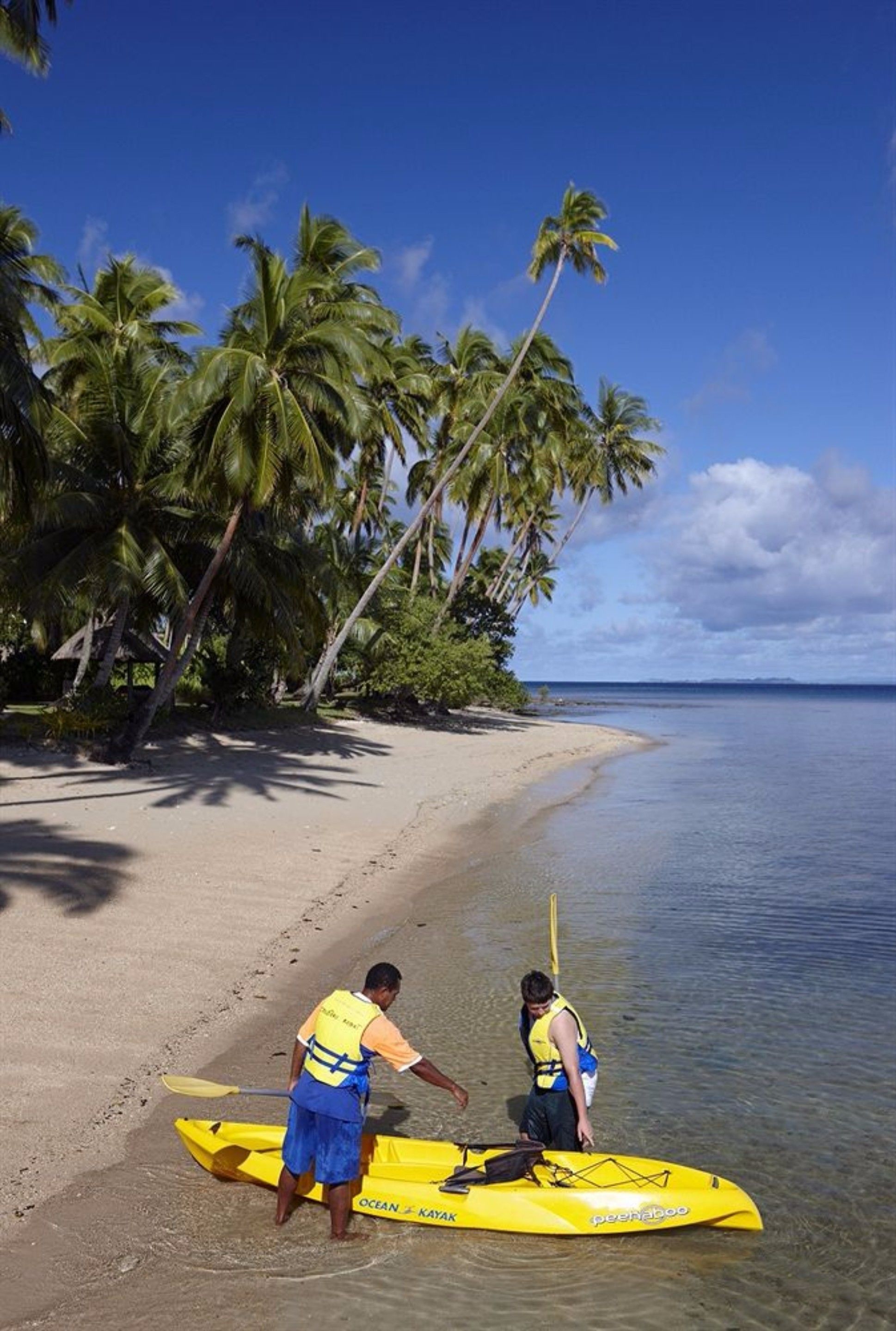 A beach with a yellow kayak and two people wearing life jackets.