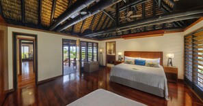 A spacious bedroom with a large bed, wooden flooring, a ceiling fan, and a view through the open door.