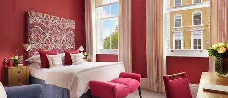 A bedroom with a large bed, a nightstand, a chair, and a window with curtains.