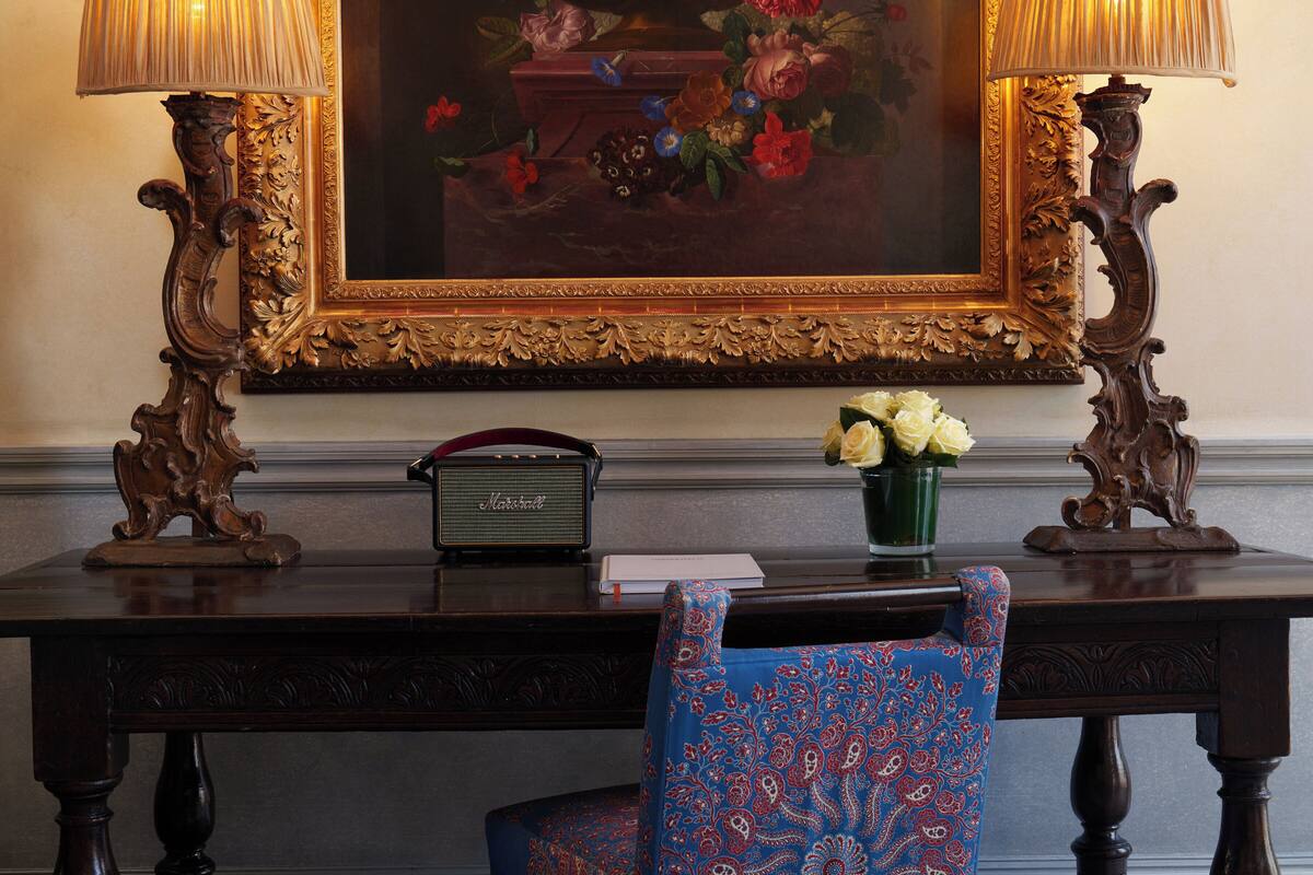 Un escritorio con una radio antigua, un florero con flores y una silla con cojín estampado.