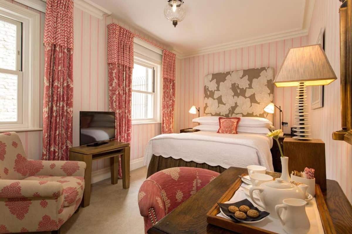 Una habitación de hotel con cama, televisor, escritorio con lámpara, silla y bandeja con té y galletas.