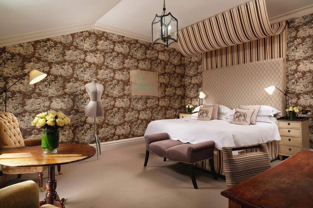 Een slaapkamer met een bed, nachtkastjes, een stoel, een lamp en een dressoir.