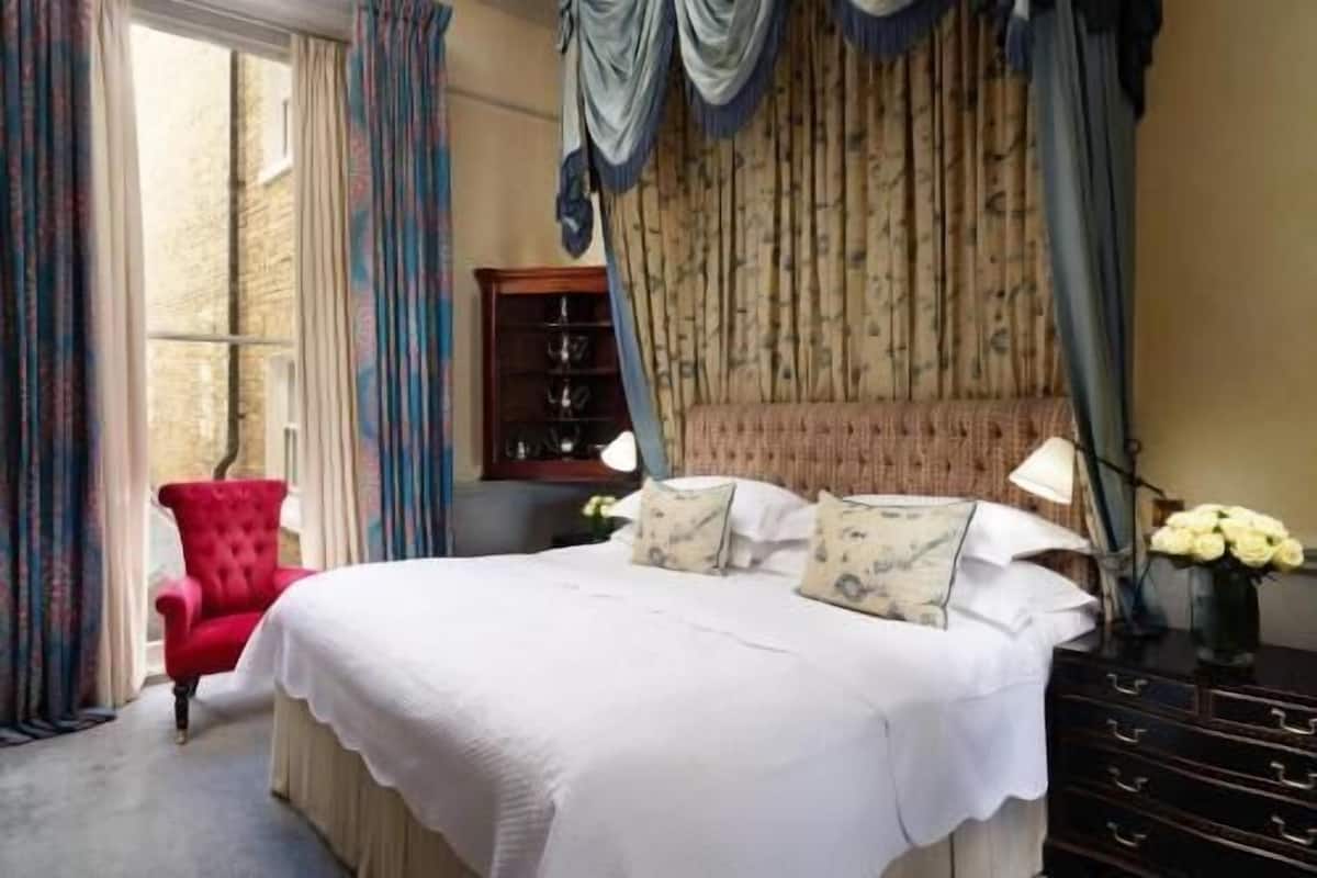 Un dormitorio con una cama grande, un sillón rojo, un armario de madera y una ventana con cortinas.