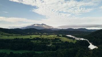 Un paisaje montañoso con un río, campos verdes y una montaña cubierta de nubes.