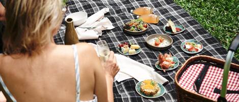 Un montaje para picnic sobre una manta de cuadros con diversos platos, una botella y una cesta.