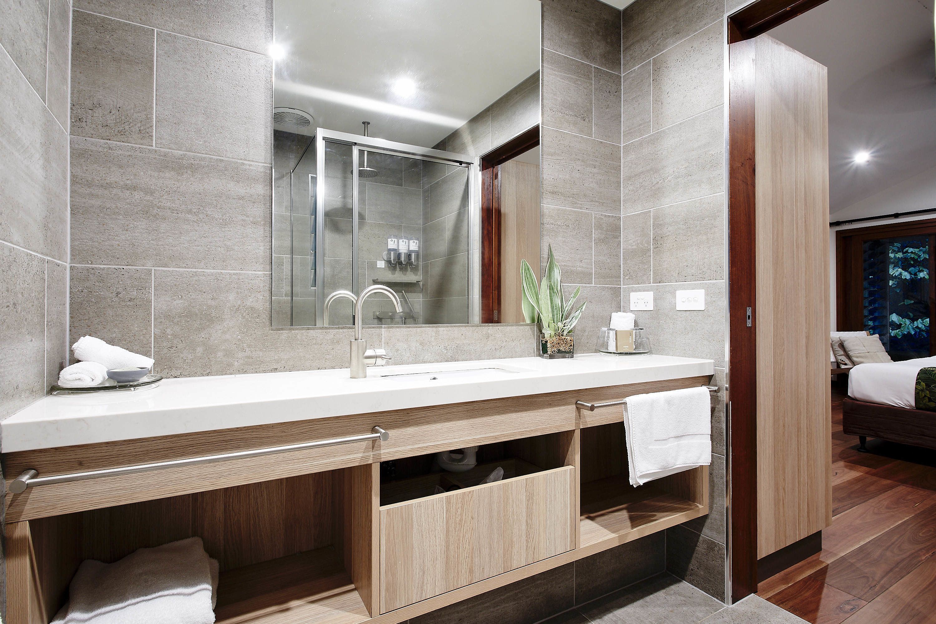 Een moderne badkamer met een grote spiegel, een douche en een wastafelmeubel met een wastafel en handdoekrek.