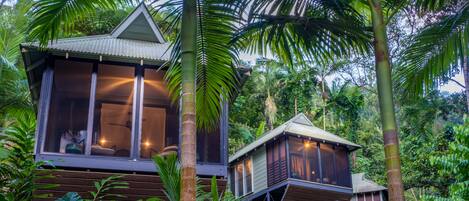 Une maison en bois dotée d’une grande fenêtre et d’un balcon, entourée d’une végétation luxuriante.