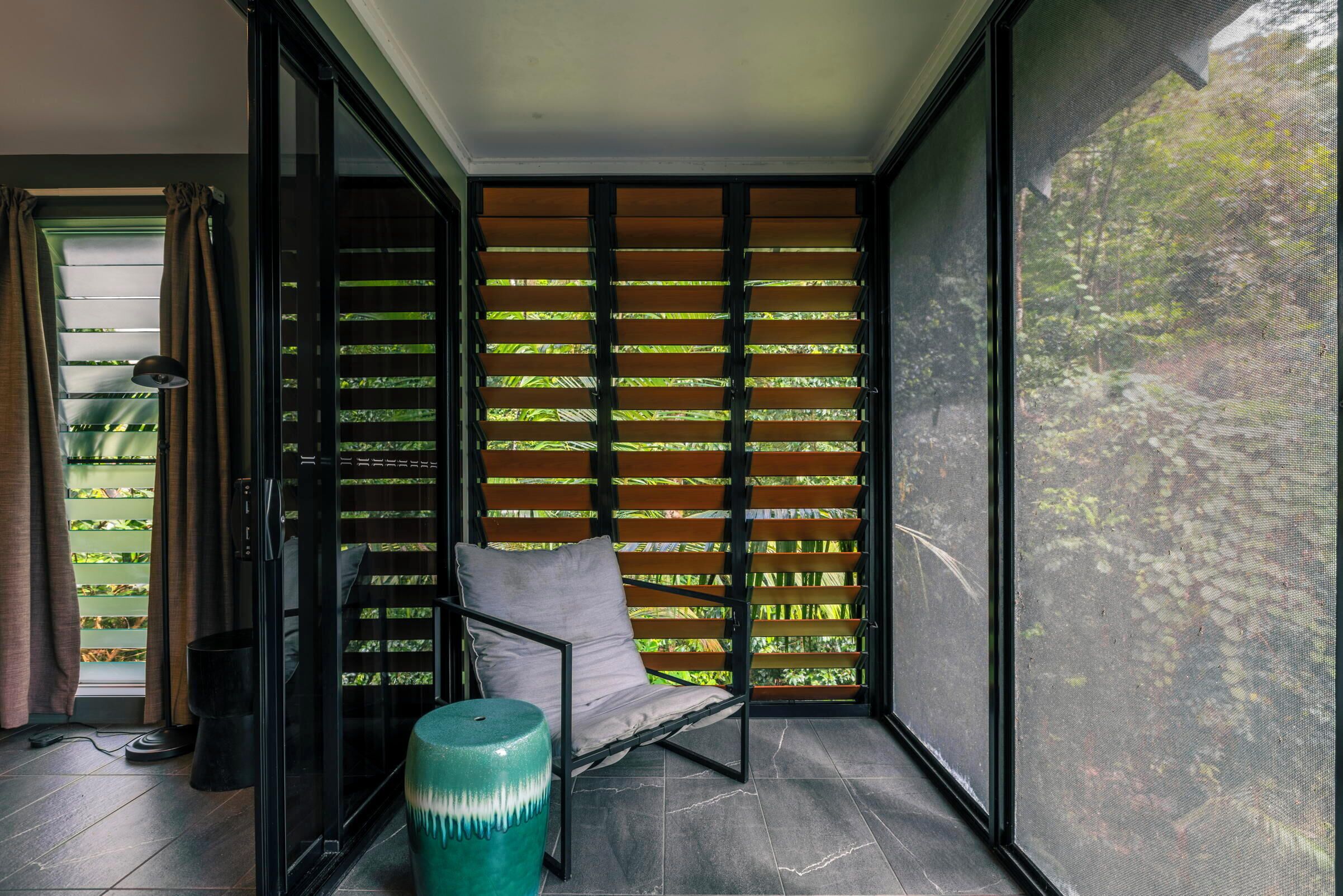 Una habitación moderna con un ventanal corredero que da a un balcón, una butaca acolchada y un adorno decorativo verde.