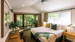 A bedroom with a large bed, bedside tables, a desk, and a chair. There is a window with curtains and a view of greenery outside. - Daintree Ecolodge (Lower Daintree)