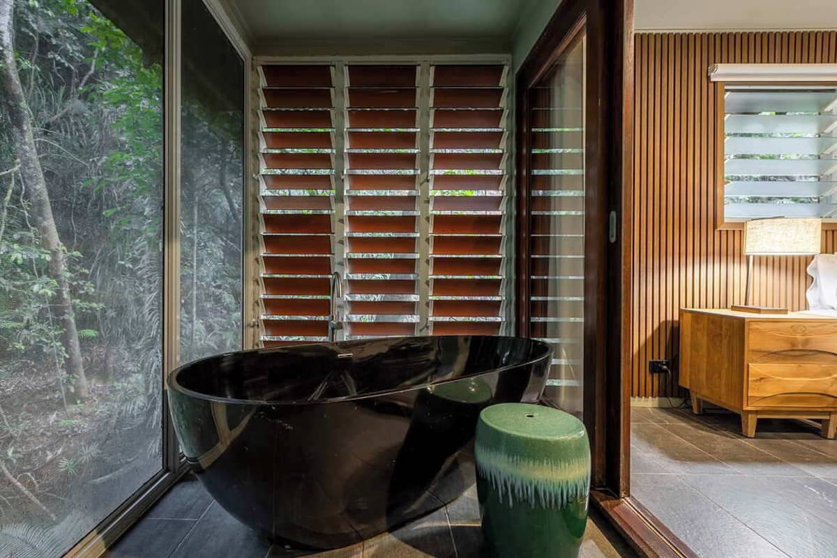 A modern bathroom with a large window, a black bathtub, and a wooden vanity.