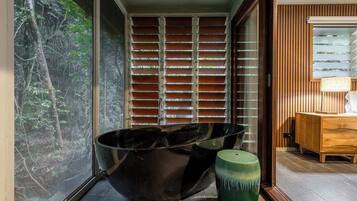 A modern bathroom with a large window, a black bathtub, and a wooden vanity.