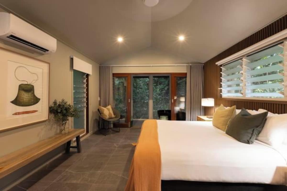 Une chambre d’hôtel avec un grand lit, un banc, une chaise et une vue sur l’extérieur par la fenêtre.