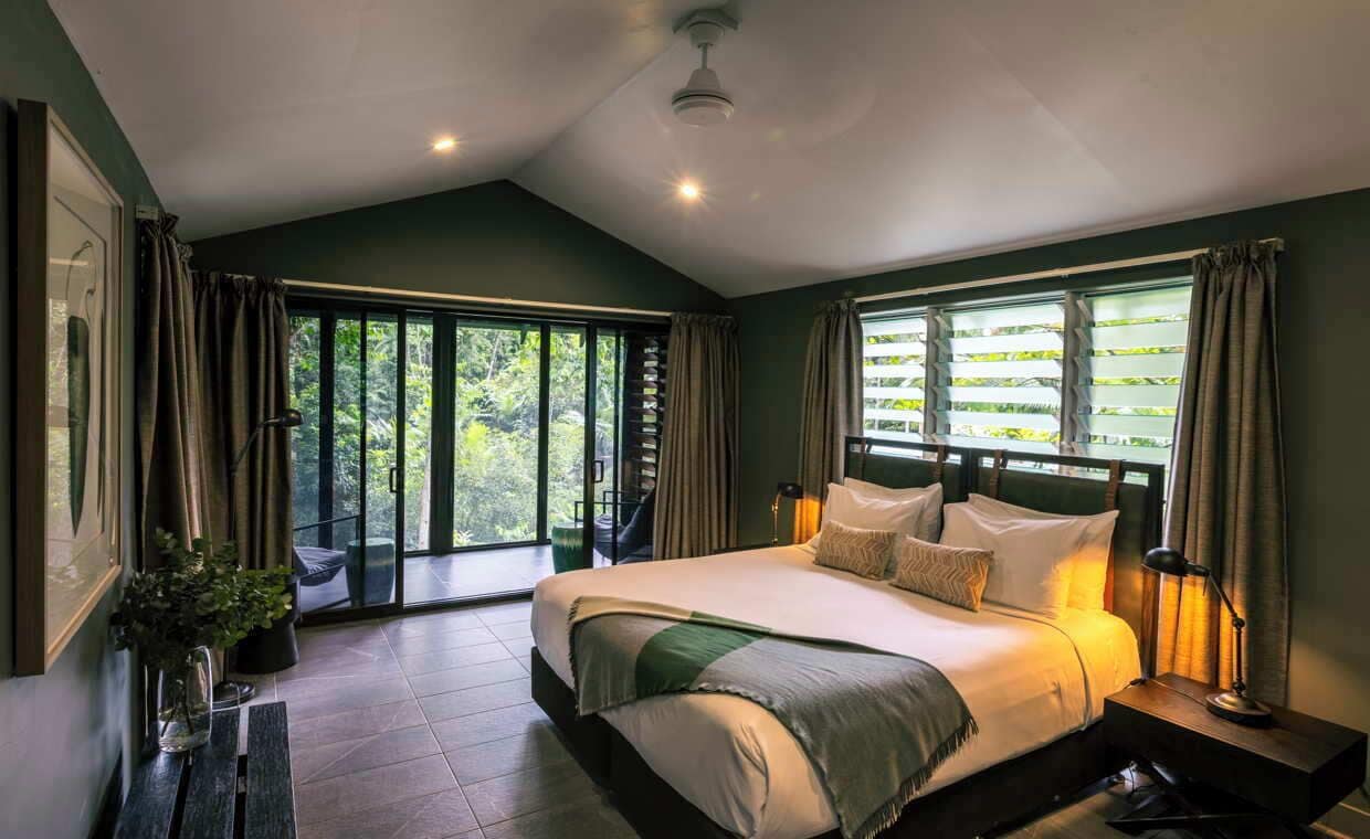 Un dormitorio amplio con una cama grande, vistas a través de puertas de cristal y un ventilador de techo.