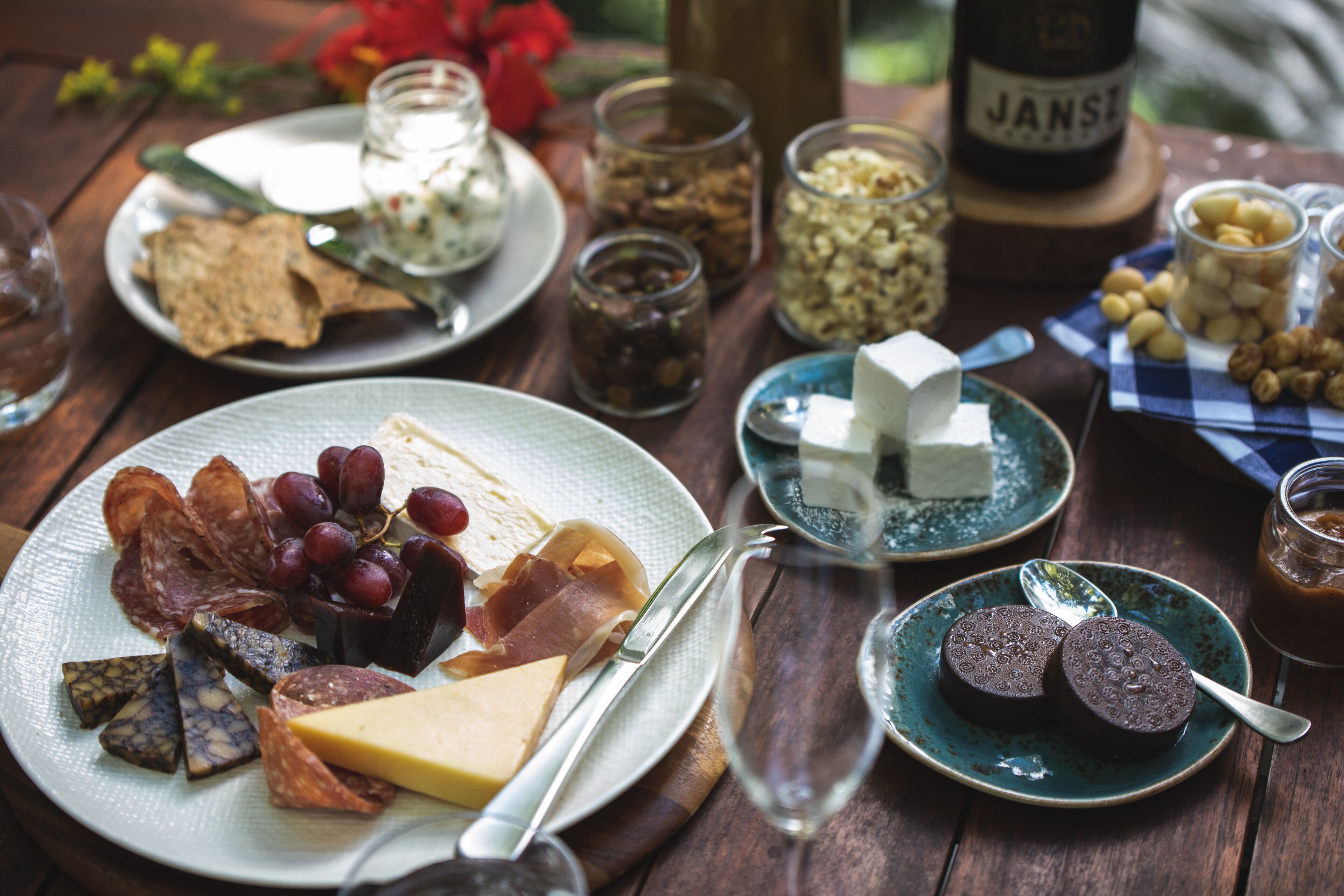 A wooden table with various food items, including cheese, meats, and nuts, accompanied by glasses and a bottle of wine.