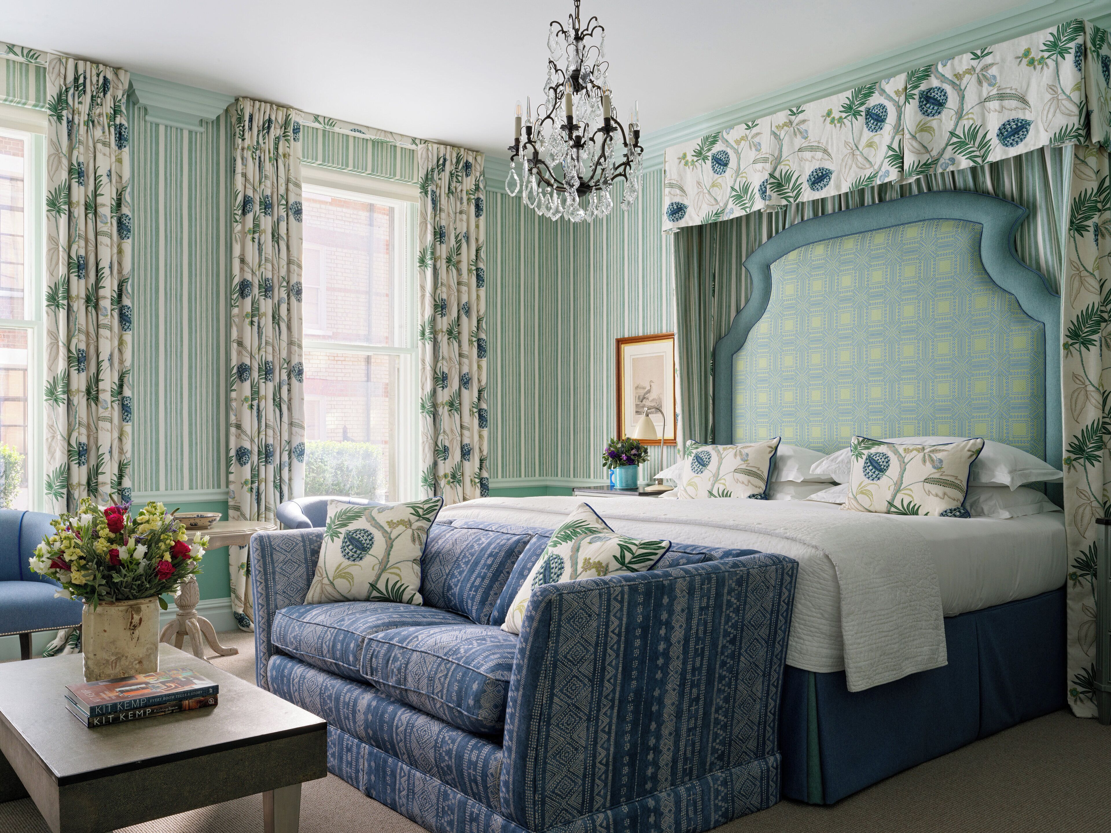 Une chambre à coucher avec un grand lit, un canapé bleu, un lustre et un papier peint à rayures.
