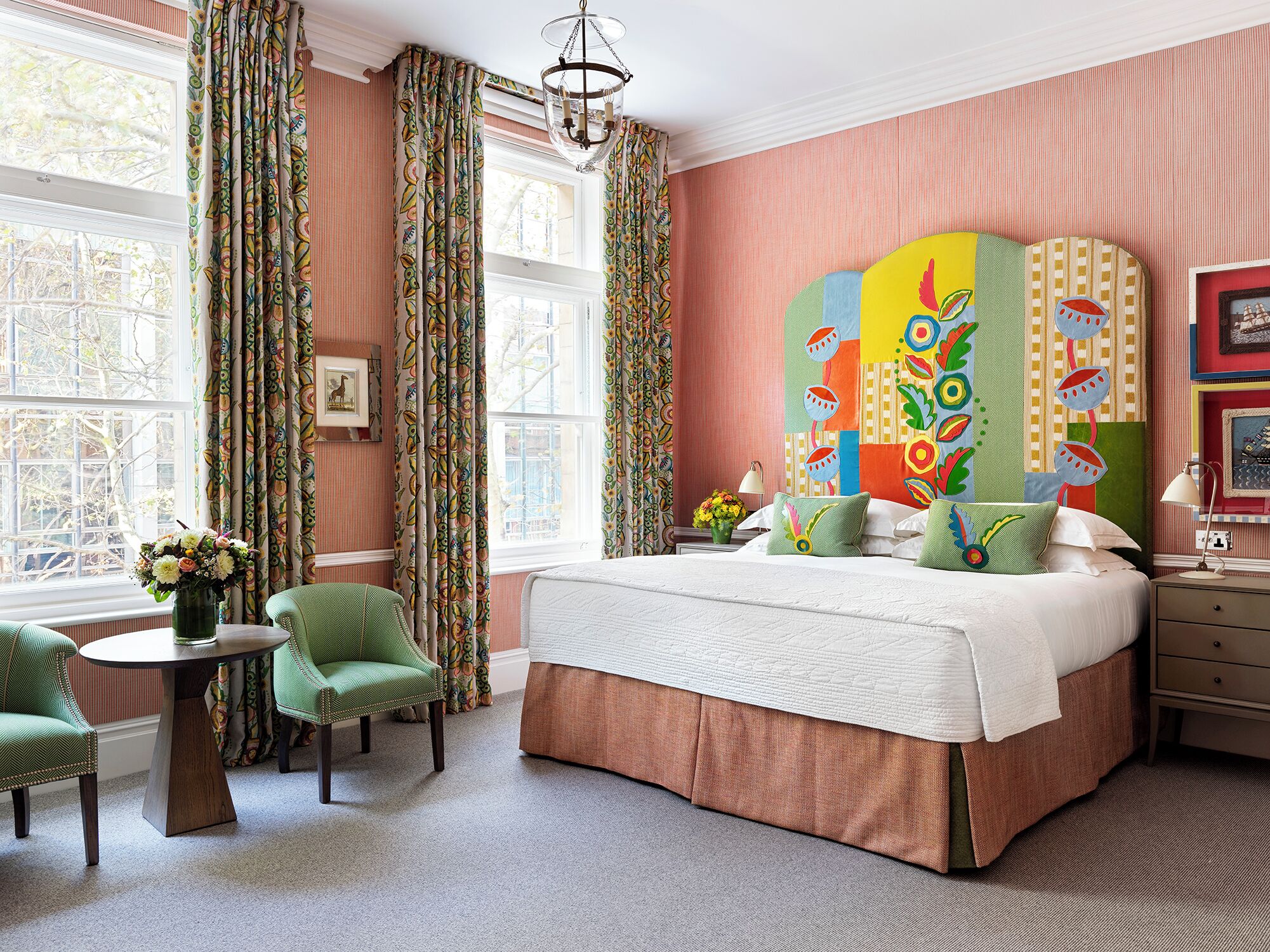 A bedroom with a large bed, a green chair, a small table, and a colorful headboard.