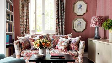 A living room with a sofa, a coffee table with a vase of flowers, a bookshelf, and a window with curtains.