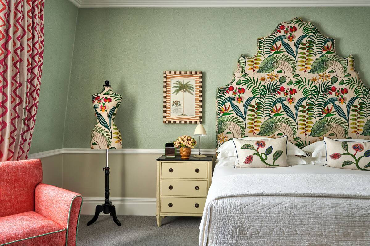 A bedroom with a bed, a nightstand, a chair, a lamp, and a wall with a tropical-themed headboard.