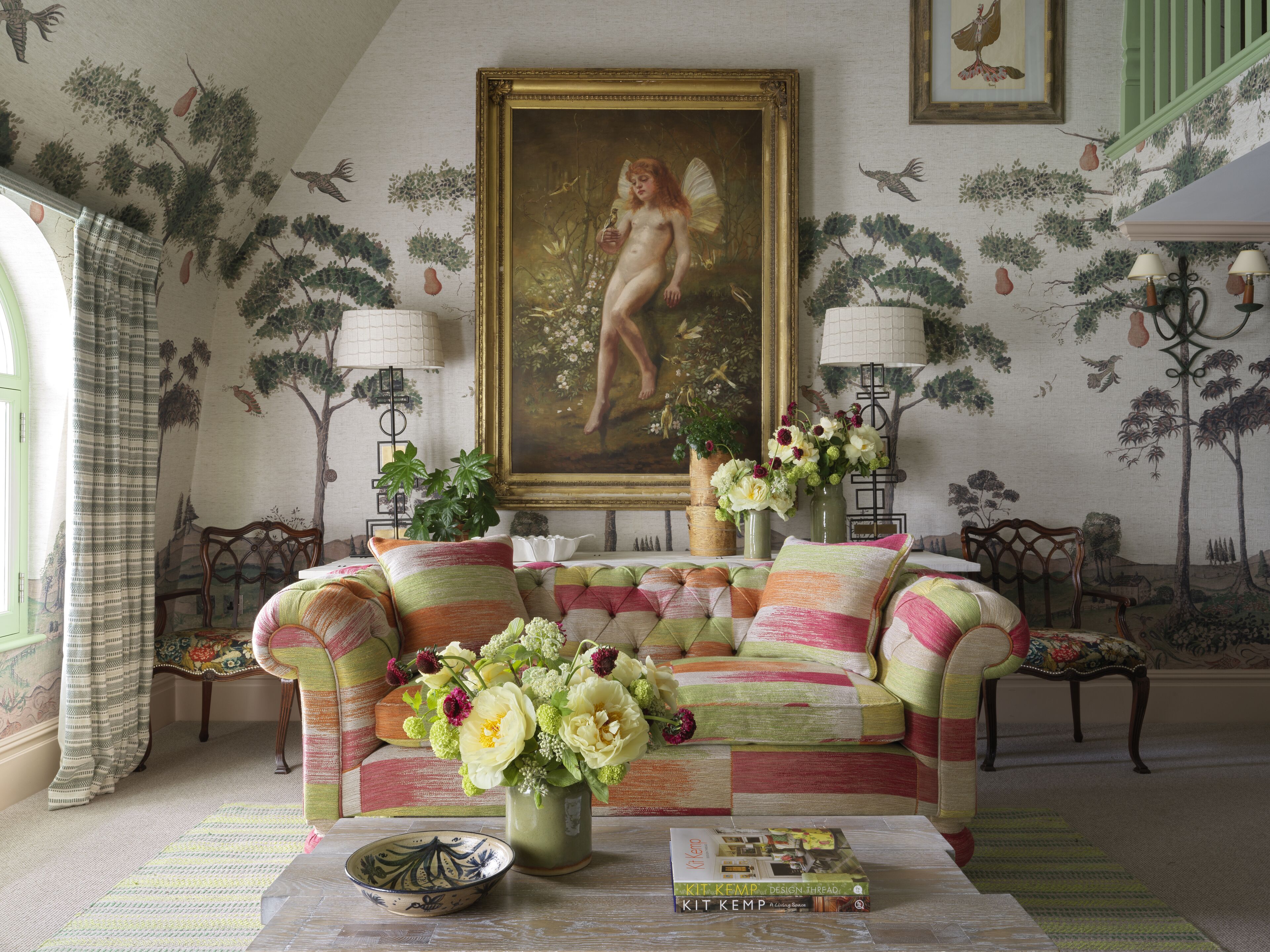 A cozy living room with a colorful sofa, a painting of a woman, and a bookshelf.
