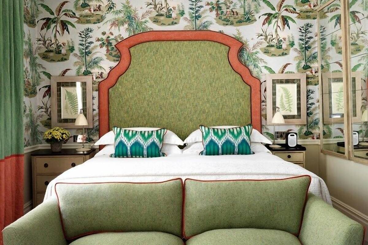 A bedroom with a large bed, green upholstered headboard, and matching green armchairs.