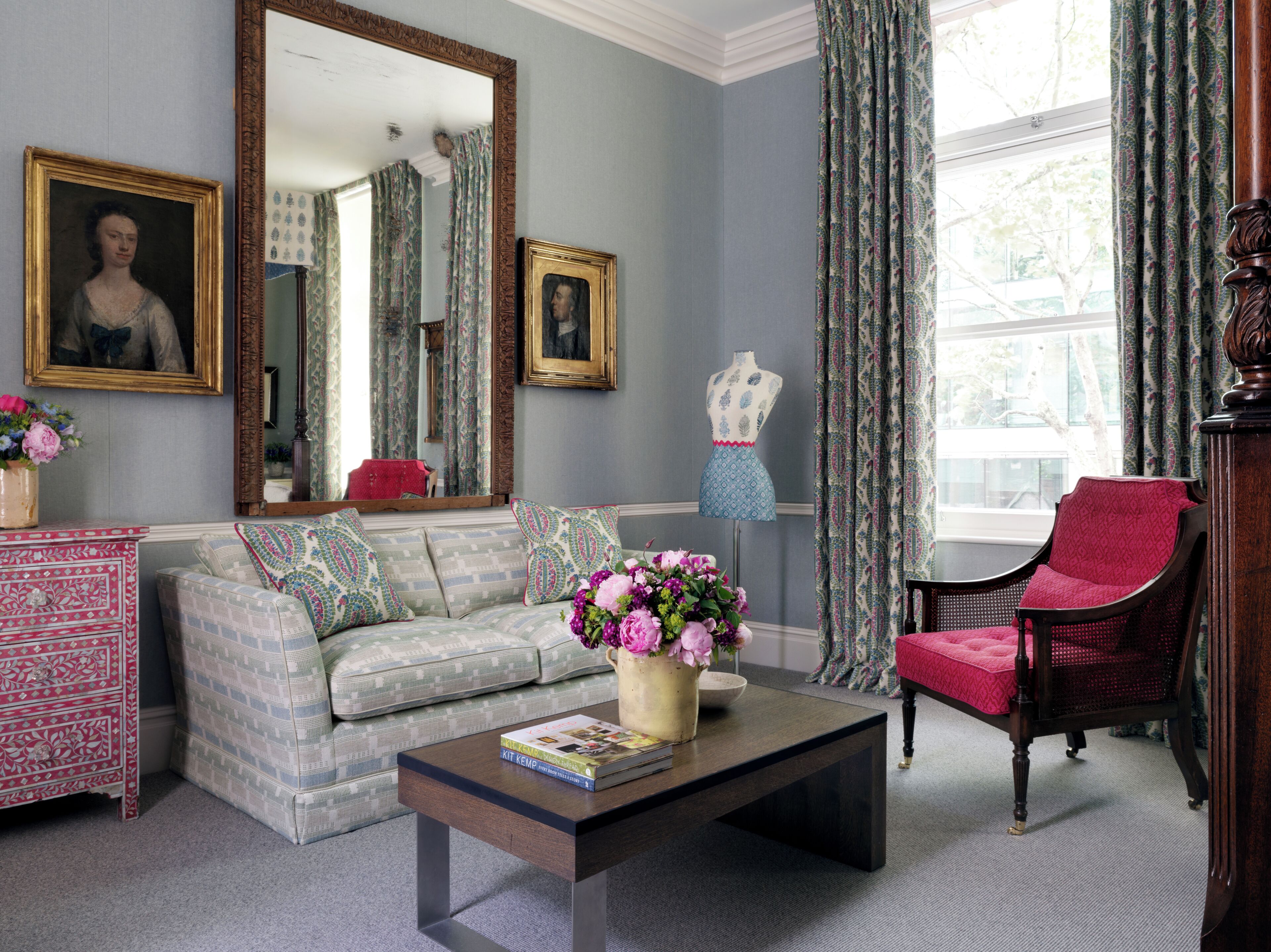 A room with a sofa, a chair, a coffee table, a dresser, a mirror, and a mannequin.