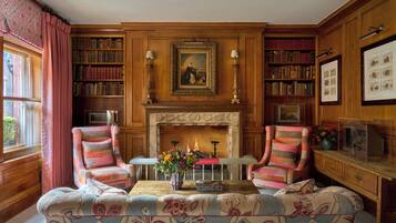 A cozy room with a fireplace, two armchairs, a sofa, and a bookshelf filled with books.